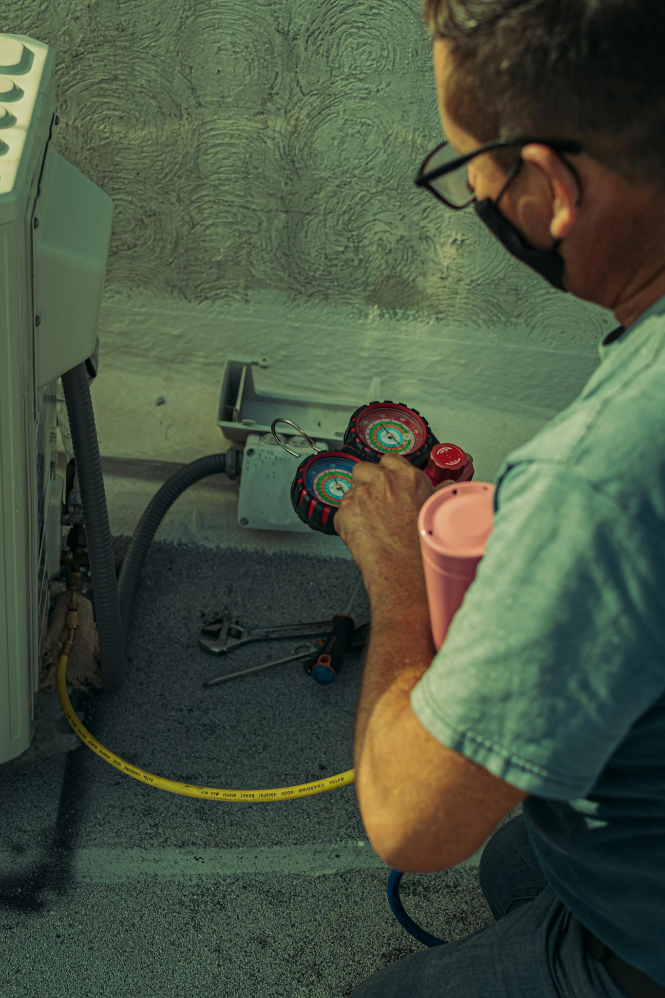 A technician checks and repairs an HVAC system outdoors using tools and gauges.